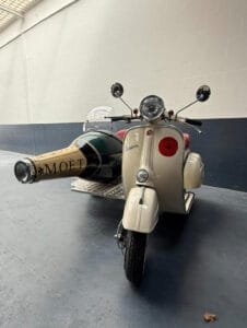 Voorkant van een Piaggio Vespa, met champagnefles als zijspan