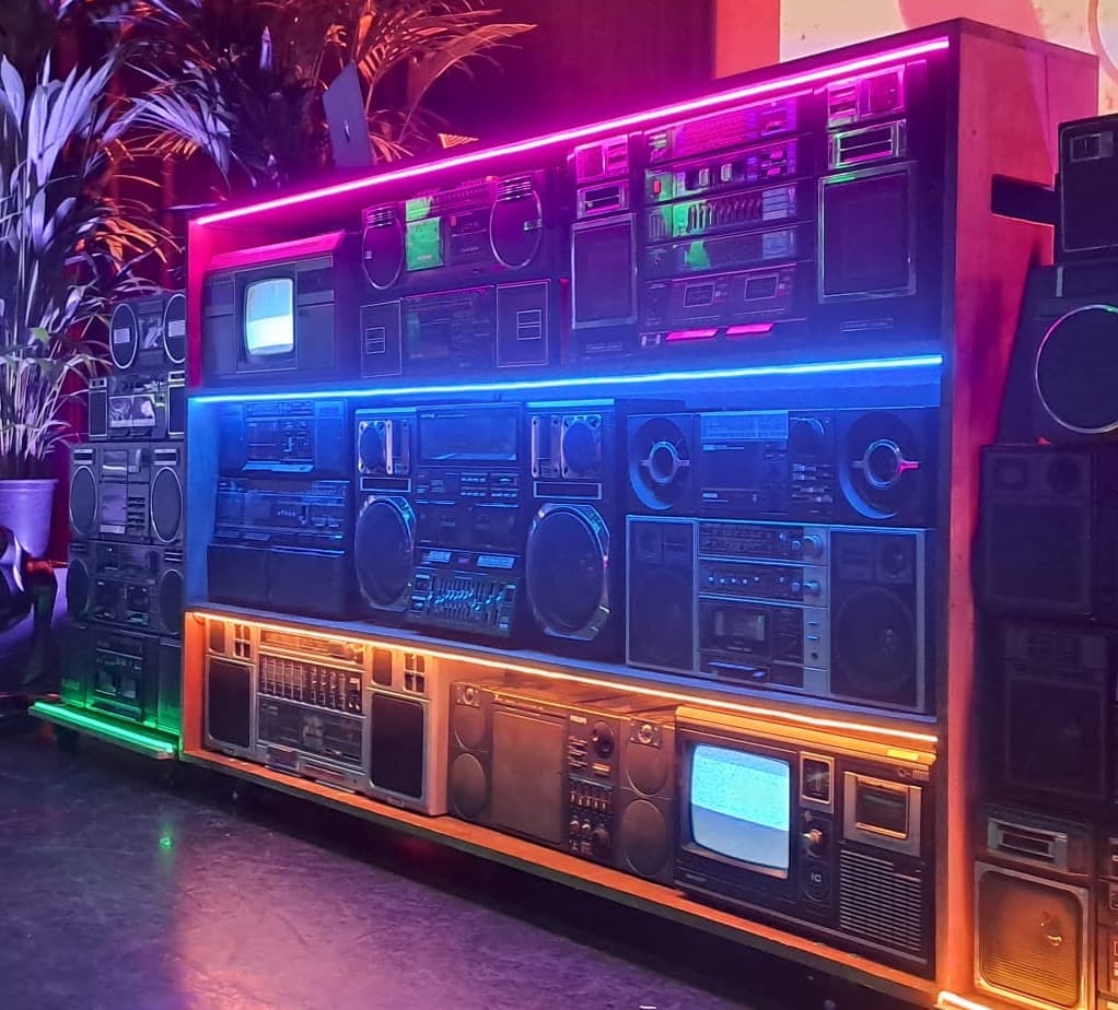 Een kast gevuld met draagbare radio cassettespelers, uitgelicht door kleurige LED verlichting, als dj booth
